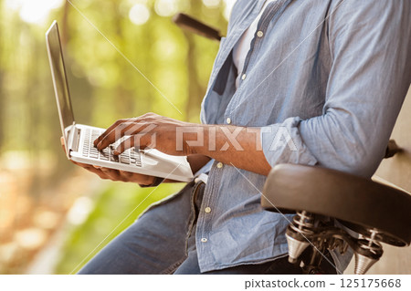 Unrecognizable black man parked bicycle and using laptop in park, cropped image, selective focus 125175668
