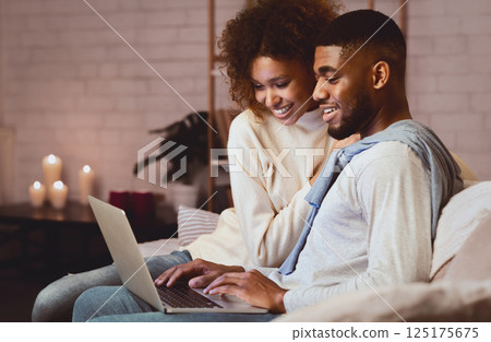 Young married couple using laptop at cozy winter evening, resting at home, free space 125175675