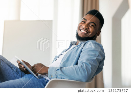 Happy african american guy using digital tablet at work and posing to camera, copy space Happy african american guy using digital tablet at work and posing to camera, copy space 125175757