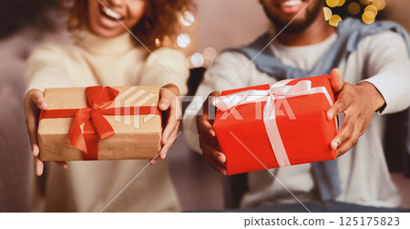 Excited afro couple holding xmas gift boxes and stretching them to camera in front of Christmas tree Excited afro couple holding xmas gift boxes and stretching them to camera in front of Christmas tree 125175823