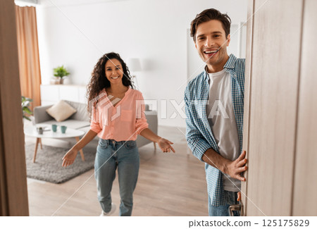 Portrait of cheerful couple welcoming inviting guests to enter home, happy young guy and lady standing in doorway of modern flat, looking out together, waiting for visitor friends to come in Portrait of cheerful couple welcoming inviting guests to enter home, happy young guy and lady standing in doorway of modern flat, looking out together, waiting for visitor friends to come in 125175829