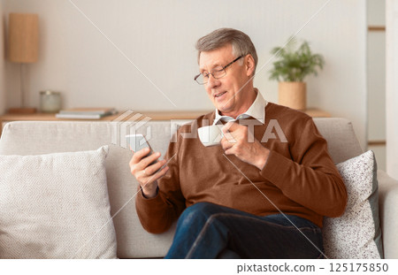 Retirement Lifestyle. Happy Senior Man Using Smartphone And Having Coffee Sitting On Couch Indoor. Selective Focus 125175850