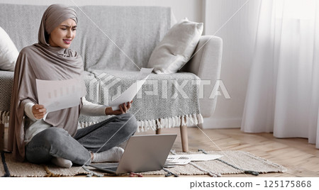I Don't Get It. Unhappy Arabic Girl In Hijab Having Problems With Her Freelance Work, Sitting Concerned On Floor With Papers And Laptop At Home I Don't Get It. Unhappy Arabic Girl In Hijab Having Problems With Her Freelance Work, Sitting Concerned On Floor With Papers And Laptop At Home 125175868
