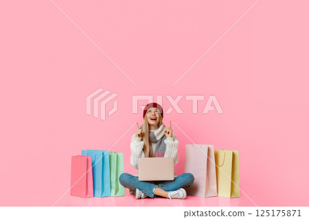 Excited pretty girl in winter clothes with laptop looking up at empty space, shopping online over yellow background Excited pretty girl in winter clothes with laptop looking up at empty space, shopping online over yellow background 125175871