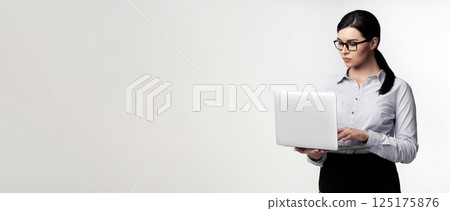 A woman in a gray shirt and black skirt uses a laptop computer in a studio. 125175876