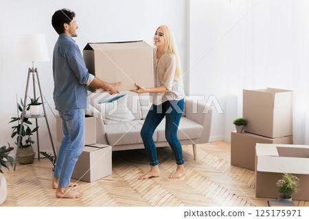 A couple moves a large cardboard box in a new apartment with bare feet and smiles. 125175971