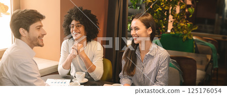 Cheerful multiethnic business partners discussing strategy of new start up project in restaurant, having lunch, copy space Cheerful multiethnic business partners discussing strategy of new start up project in restaurant, having lunch, copy space 125176054