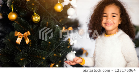 Christmas time. Adorable african american girl smiling near Xmas tree at home, empty space Christmas time. Adorable african american girl smiling near Xmas tree at home, empty space 125176064