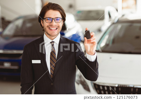 Successful Salesperson. Handsome Agent In Specs Showing Auto Key Standing In Automobile Rental Office, Free Space Successful Salesperson. Handsome Agent In Specs Showing Auto Key Standing In Automobile Rental Office, Free Space 125176073
