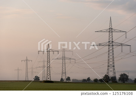 Electricity pylons in a row over the agricultural fields on a foggy morning 125176108