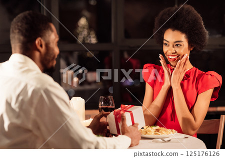 Valentine's Day. African American Man Giving A Gift To Girlfriend Having Romantic Date In Restaurant. Selective Focus Valentine's Day. African American Man Giving A Gift To Girlfriend Having Romantic Date In Restaurant. Selective Focus 125176126