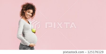 Healthy nutrition. Happy expectant woman holding apple and touching belly over pink background 125176129