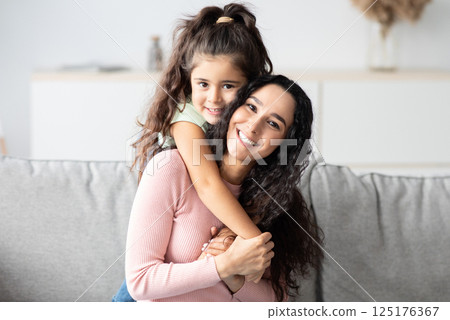 Portraif Of Cute Little Girl And Her Mom Embracing At Home, Young Mother Enjoying Spending Time With Her Child, Loving Kid Hugging Mom While They Relaxing On Couch In Living Room, Copy Space Portraif Of Cute Little Girl And Her Mom Embracing At Home, Young Mother Enjoying Spending Time With Her Child, Loving Kid Hugging Mom While They Relaxing On Couch In Living Room, Copy Space 125176367