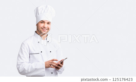 Culinary App. Smiling Chef Man Using Smartphone Standing Over White Studio Background. Panorama Culinary App. Smiling Chef Man Using Smartphone Standing Over White Studio Background. Panorama 125176423