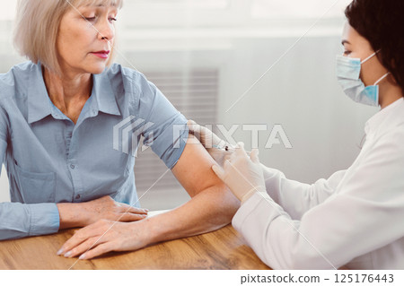 Immunization. Young female mexican doctor injecting vaccine to senior woman at clinic office, copyspace 125176443