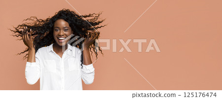 A young African American woman with long curly black hair is smiling at the camera. Her hair is flowing freely around her head and she is wearing a white collared shirt. A young African American woman with long curly black hair is smiling at the camera. Her hair is flowing freely around her head and she is wearing a white collared shirt. 125176474