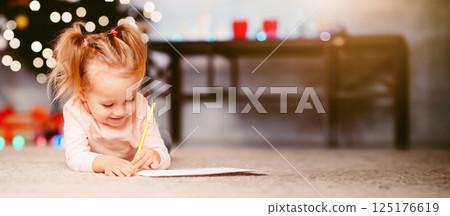 Cute baby girl drawing wishlist near Christmas tree at home, free space 125176619