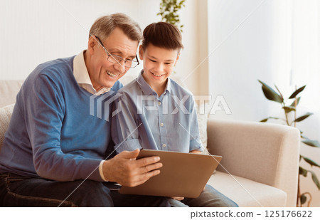Grandfather And Grandson Using Laptop Together Watching Movie Or Browsing Internet Sitting On Couch Indoor. Free Space 125176622
