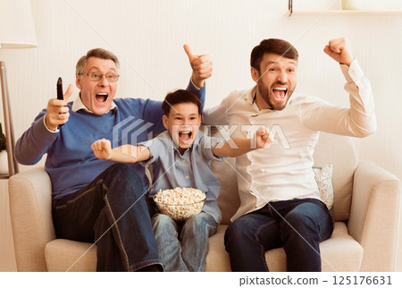 Soccer Fans. Happy Son, Father And Grandpa Watching Sport Match On TV Celebrating Victory Sitting On Sofa At Home. Soccer Fans. Happy Son, Father And Grandpa Watching Sport Match On TV Celebrating Victory Sitting On Sofa At Home. 125176631