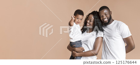 Happy family. Portrait of young african american parents holding cute little son on hands over yellow studio background, copy space 125176644