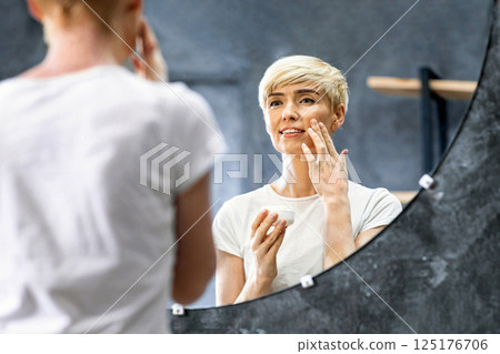 Caring For Skin. Cheerful Mature Woman Applying Facial Cream Preventing Aging And Wrinkles Standing In Bathroom At Home. Selective Focus 125176706