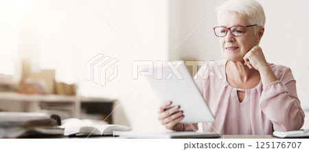Smiling beautiful senior woman with glasses using digital tablet at home, empty space 125176707