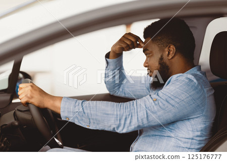 Depressed African Man Sitting In Driver's Seat Of New Too Expensive Car, Thinking Of Money Problems In Auto Dealership Store 125176777