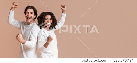 We made it. Joyful multiracial couple celebrating success, raising fists, rejoicing victory together over yellow background with free space We made it. Joyful multiracial couple celebrating success, raising fists, rejoicing victory together over yellow background with free space 125176784