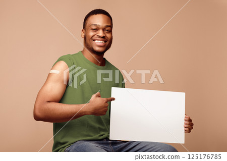 Covid-19 Vaccination. Vaccinated Black Man Holding Empty Poster For Coronavirus Vaccine Advertisement Sitting Over Beige Studio Background, Smiling To Camera. Corona Virus Prevention. Mockup Covid-19 Vaccination. Vaccinated Black Man Holding Empty Poster For Coronavirus Vaccine Advertisement Sitting Over Beige Studio Background, Smiling To Camera. Corona Virus Prevention. Mockup 125176785