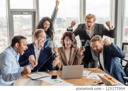 A group of six colleagues in business attire celebrate a success in a modern office with large windows. They are all excited and raise their fists in the air A group of six colleagues in business attire celebrate a success in a modern office with large windows. They are all excited and raise their fists in the air 125177004