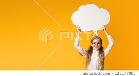 Smiling Elementary Student Girl Holding Speech Bubble Overhead On Yellow Studio Background. Thinking Of School. Mockup, Free Space 125177005