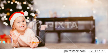 Cozy Christmas evening. Little girl drawing on floor near xmas tree, free space 125177143