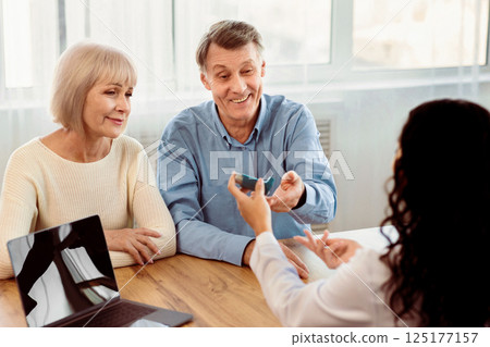 Asthma Treatment. Female doctor giving blue inhaler to senior patient who is sitting with his mature wife, copyspace 125177157