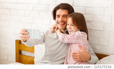 Positive hugging father and little daughter taking selfie on smartphone at home, free space 125177210