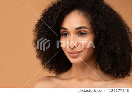 African American woman with curly, black hair looks to the right, smiling softly. She has a tan complexion and is wearing no makeup, highlighting her natural beauty. 125177348