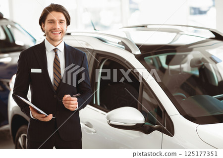 Car Sales. Handsome Salesman Selling Automobile Standing Near New Auto, Holding Pen And Clipboard Car Sales. Handsome Salesman Selling Automobile Standing Near New Auto, Holding Pen And Clipboard 125177351