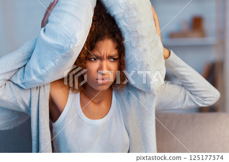 Annoyed woman covering ears with pillow, suffering from noisy neighbours 125177374