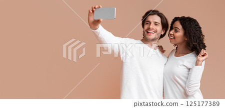 Say Cheese. Cheerful interracial couple taking sellfie on smartphone together, posing over yellow background with free space Say Cheese. Cheerful interracial couple taking sellfie on smartphone together, posing over yellow background with free space 125177389