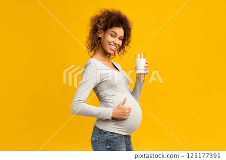 Pregnancy and calcium. Afro woman with glass of milk showing thumb up over pink studio background 125177391