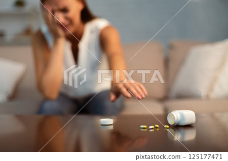 Depression. Suicidal Girl Reaching After Antidepressant Or Sleeping Pills Sitting On Couch Indoor. Selective Focus, Shallow Depth 125177471