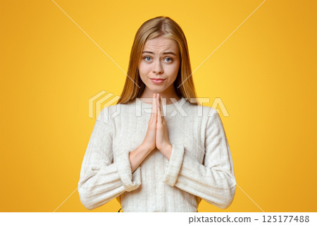 Cherished wish. Beautiful millennial girl praying with hands clasped near face, orange studio background with empty space Cherished wish. Beautiful millennial girl praying with hands clasped near face, orange studio background with empty space 125177488