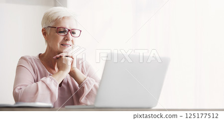 Senior excited woman reading article online, using laptop at home, free space 125177512