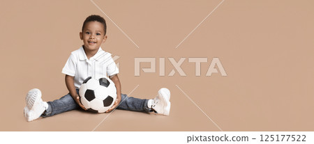Football classes for children. Portrait of cute black boy with soccer ball sitting over yellow studio background, free space Football classes for children. Portrait of cute black boy with soccer ball sitting over yellow studio background, free space 125177522