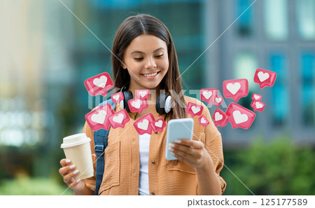 A young woman smiles as she uses her smartphone. Social media icons in the shape of hearts are surrounding her, symbolizing the popularity of the content she is creating or viewing A young woman smiles as she uses her smartphone. Social media icons in the shape of hearts are surrounding her, symbolizing the popularity of the content she is creating or viewing 125177589