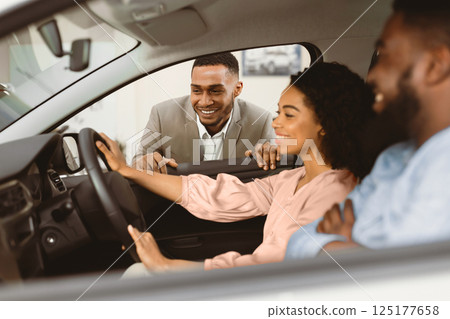 Car Sales. Black Couple Choosing New Vehicle Talking With Dealer Sitting In Auto In Dealership Shop. Selective Focus 125177658
