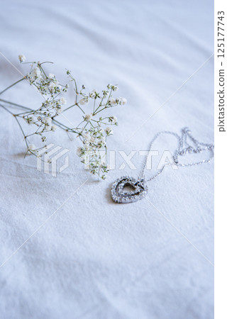 Heart-shaped pendant necklace on delicate white fabric with baby's breath floral accent 125177743