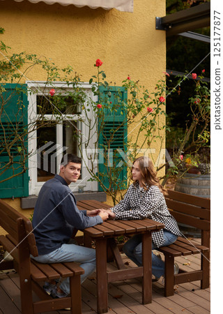 Romantic Garden Picnic: Couple Holding Hands at Vintage Yellow Building with Green Shutters and Rose Garden. Intimate Outdoor Moment Captures Love and Architectural Charm in Picturesque Romantic Romantic Garden Picnic: Couple Holding Hands at Vintage Yellow Building with Green Shutters and Rose Garden. Intimate Outdoor Moment Captures Love and Architectural Charm in Picturesque Romantic 125177877