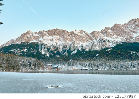 Picturesque Alpine Ski Resort Nestled between Frozen Lake and Snow Covered Mountain Peaks with Traditional Wooden Chalets Reflecting in Crystal Clear Water Surface during Winter Season in European Picturesque Alpine Ski Resort Nestled between Frozen Lake and Snow Covered Mountain Peaks with Traditional Wooden Chalets Reflecting in Crystal Clear Water Surface during Winter Season in European 125177987