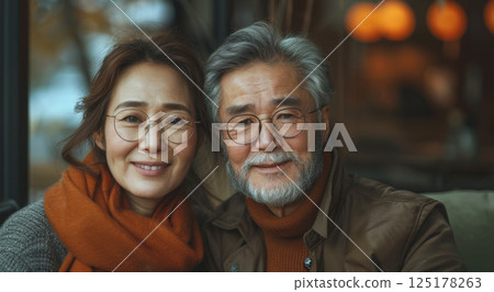 A couple wearing glasses smiles warmly at the camera while sitting in a cafe. 125178263
