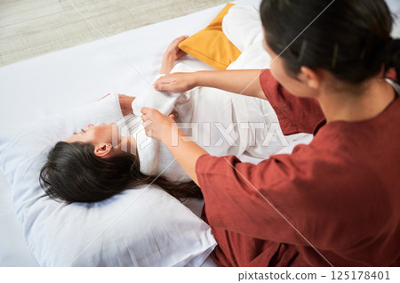 Masseuse making thai yoga massage. Woman therapist doing traditional massage treatment for female patient. Client lying on mat, meditating, enjoying hand massage in calm atmosphere. Cropped view. 125178401
